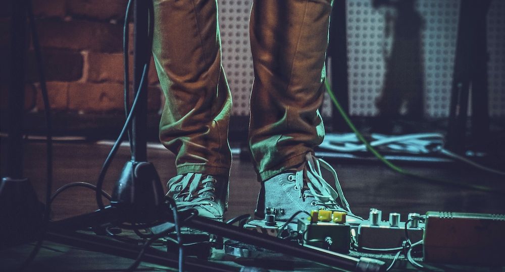 Closeup of the feet of a person near guitar pedals and a mic stand under the lights