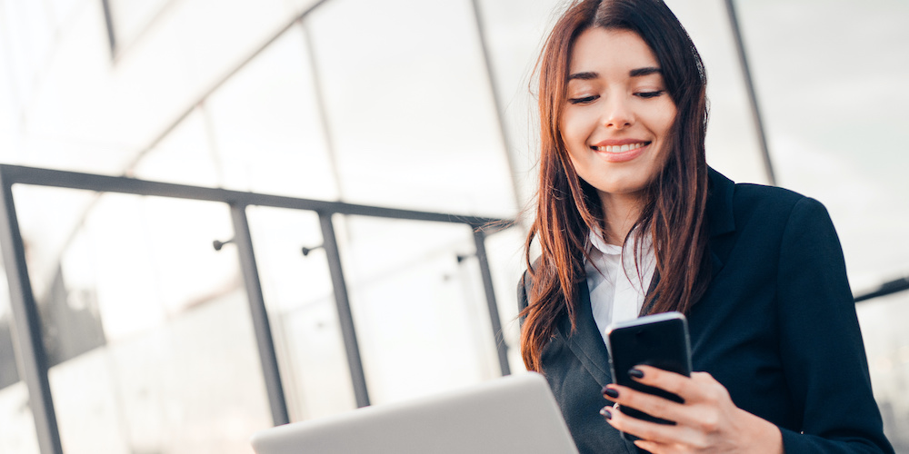 Successful smiling businesswoman or entrepreneur using laptop and phone sitting in front of his office.